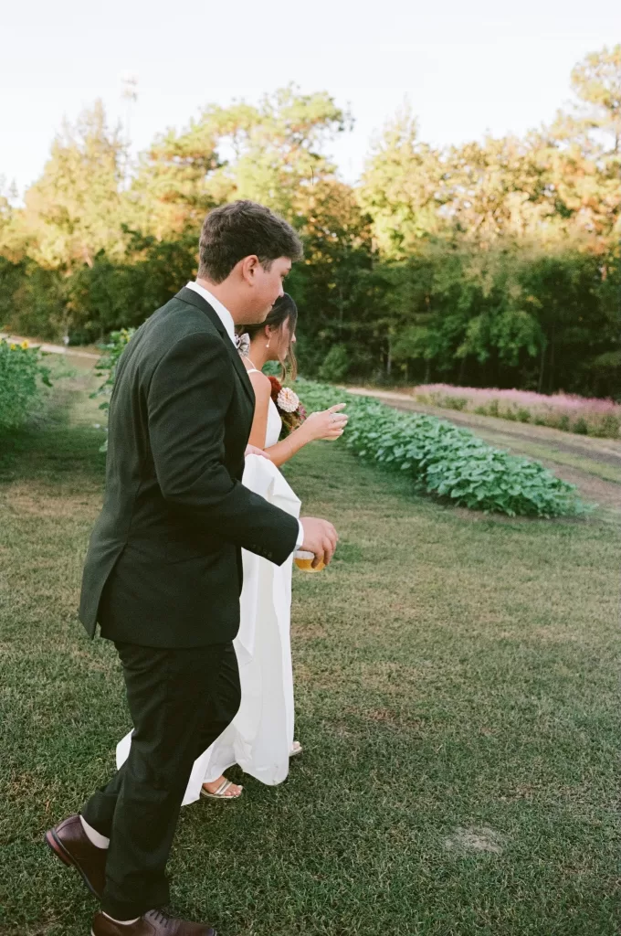 The newlyweds walk across the lawn at The Greenhouse at Arrows Farm during golden hour, holding drinks and enjoying a quiet moment.