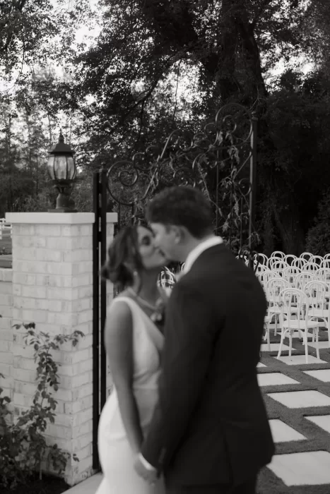A soft black and white portrait of the couple kissing near the ceremony gates at The Greenhouse at Arrows Farm.