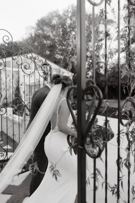 The couple walk through the iron gates at The Greenhouse at Arrows Farm, captured in an intimate black and white moment.