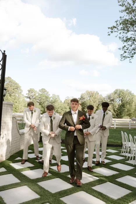 Groomsmen walk across the patterned garden aisle at The Greenhouse at Arrows Farm before the outdoor ceremony.