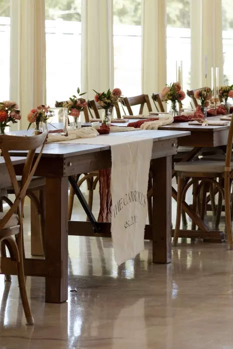 Long wooden reception tables styled with florals and linens inside The Greenhouse at Arrows Farm, filled with natural light.