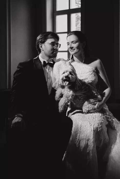 Black and white wedding portrait of a couple seated together with their dog, capturing a quiet and personal moment.