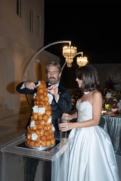 Bride and groom cutting a croquembouche cake during an evening wedding reception at Islet Santorini under sculptural lights.