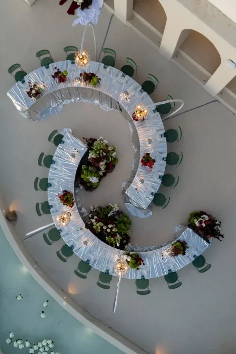 Overhead view of a curved wedding reception table set above the water at Islet Santorini with modern florals and sculptural lighting.