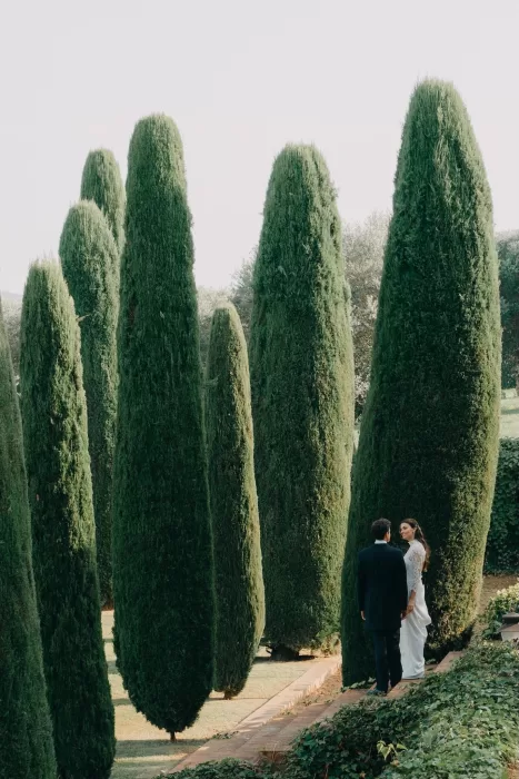 Couple standing between tall cypress trees in the gardens of Mas de Les Voltes, creating a timeless and romantic scene.