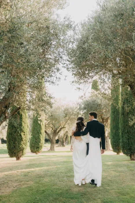 Bride and groom walking arm in arm through the olive trees at Mas de Les Voltes, capturing a calm and romantic atmosphere.