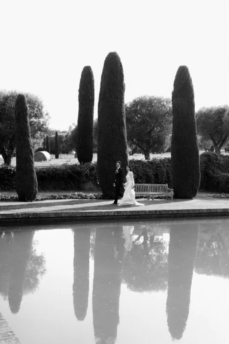 Bride and groom walking beside the reflecting pool at Mas de Les Voltes in a timeless black and white moment.