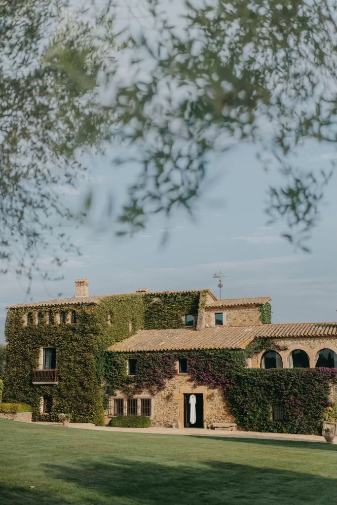 Rustic stone facade of Mas de Les Voltes covered in ivy, with the wedding dress hanging in the doorway before the ceremony.