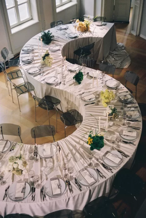 Modern wedding reception table arranged in a curved layout with minimalist florals and candlelight, photographed in an editorial style.