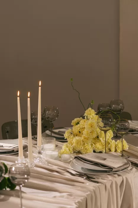 Wedding table styled with pale florals, glassware, and tall candles, creating a calm and modern tablescape.