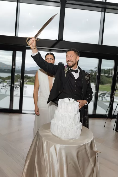Groom cutting the wedding cake with a ceremonial sword during the reception at Boturich Castle.