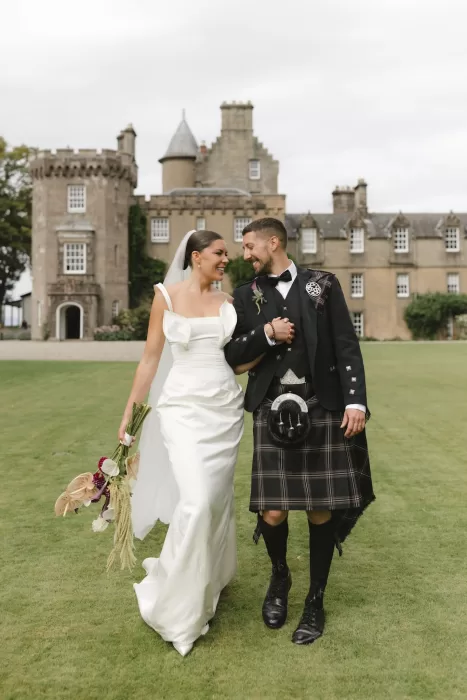 Bride and groom walking together across the lawn in front of Boturich Castle after the ceremony.