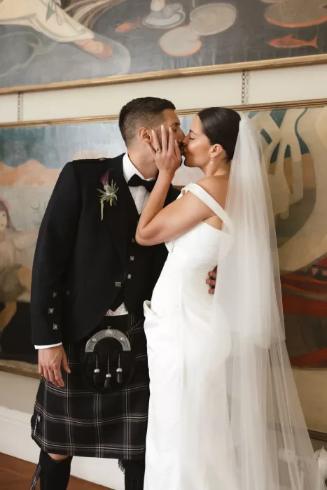 Bride and groom sharing a kiss indoors at Boturich Castle, framed by historic artwork.