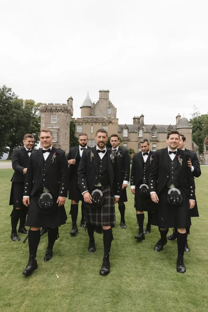 Groomsmen walking across the lawns in traditional attire at Boturich Castle.
