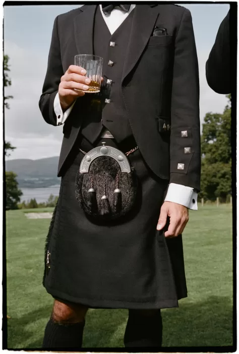 Groom wearing a traditional kilt and sporran while holding a drink on the lawn at Boturich Castle.