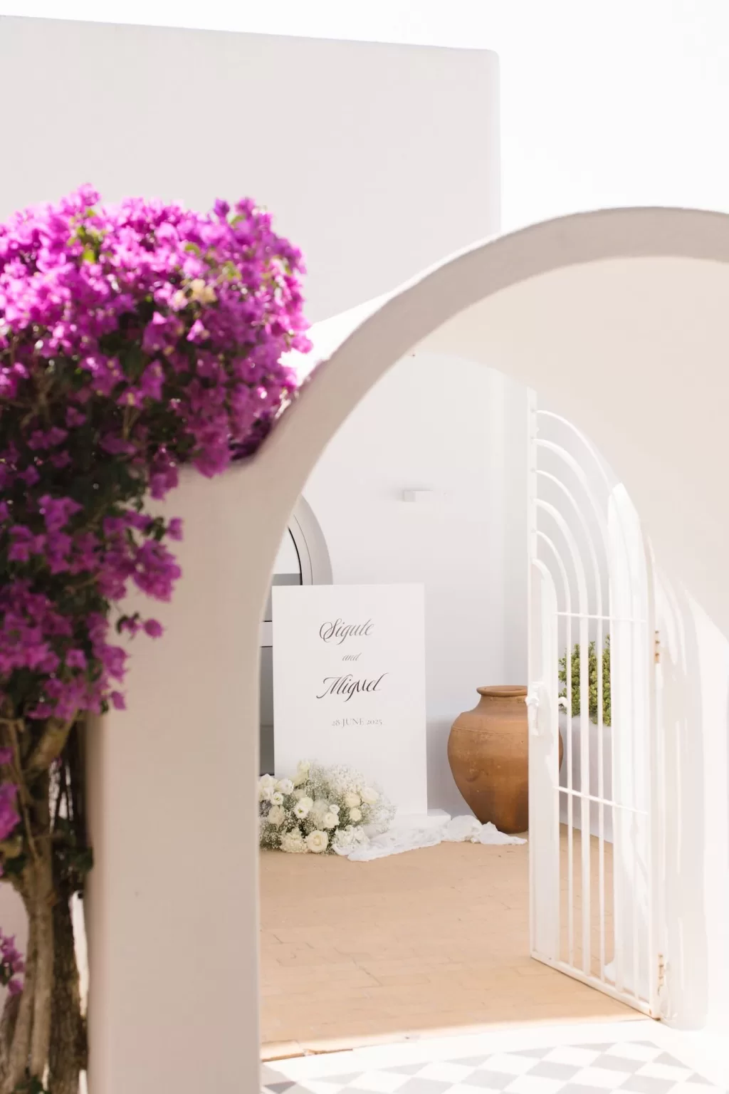Bougainvillea-framed archway at Casa Arte leading to a wedding welcome sign and white floral arrangements.