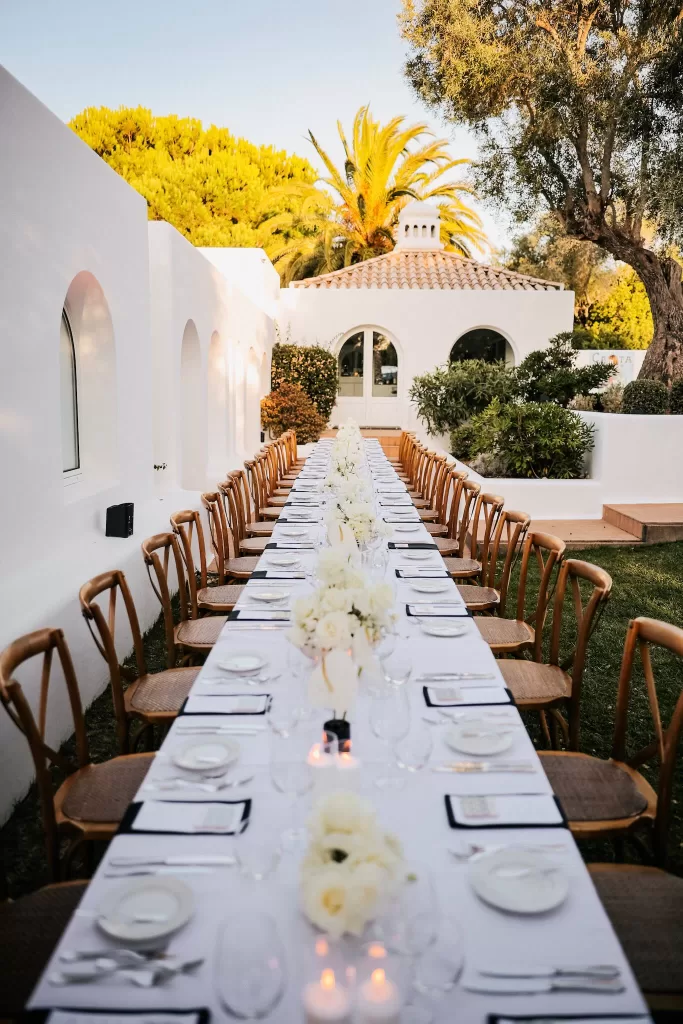 Long outdoor wedding dining table at Casa Arte Lagos set between white arches and lush gardens during golden hour.