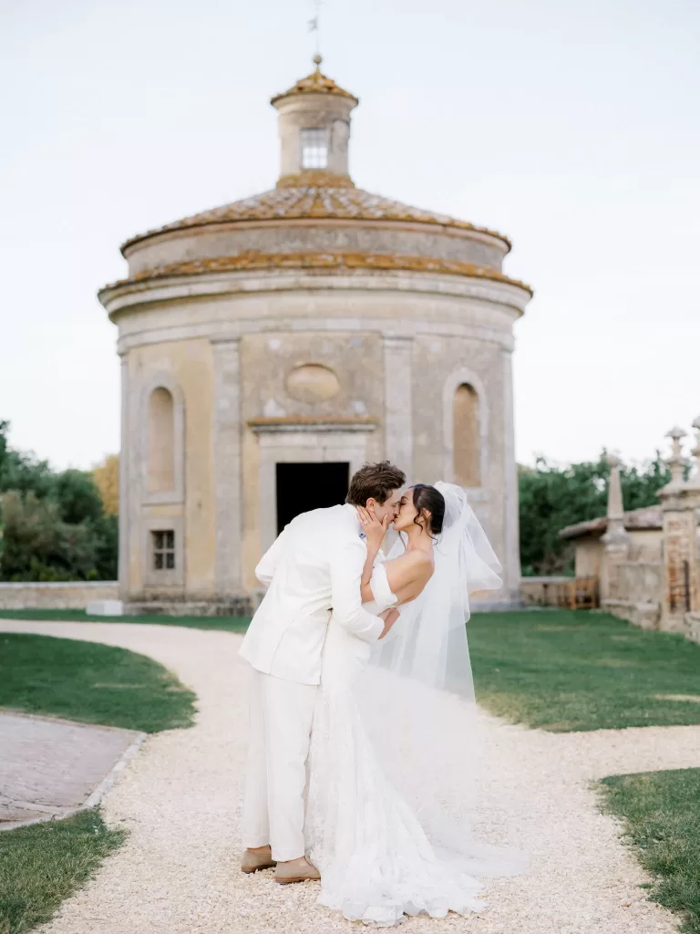 Newlyweds sharing a kiss in front of the iconic round chapel at Castello di Celsa at sunset.