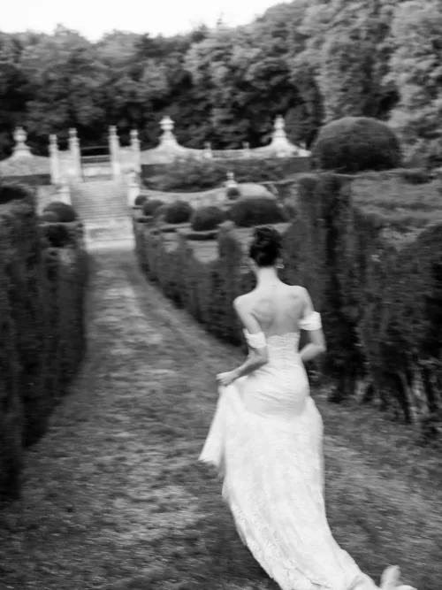 Bride walking through the formal Italian gardens at Castello di Celsa with sculpted hedges and grand stone staircase.