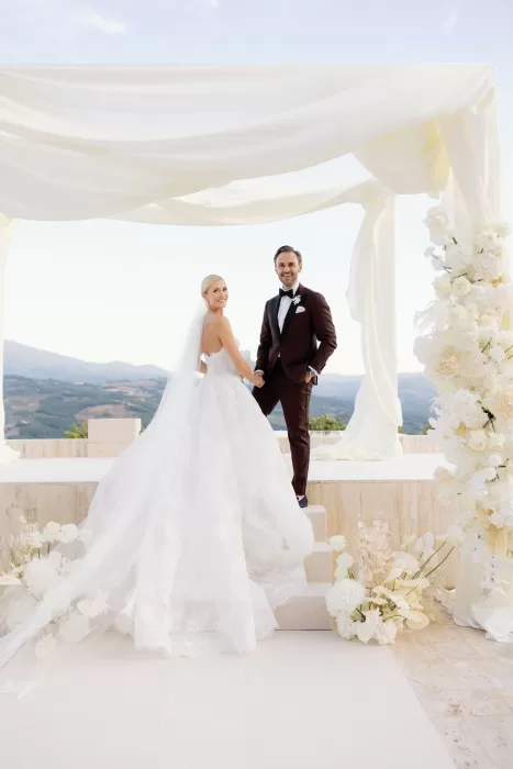 Bride and groom holding hands on ceremony steps framed by white florals at Castello di Velona.