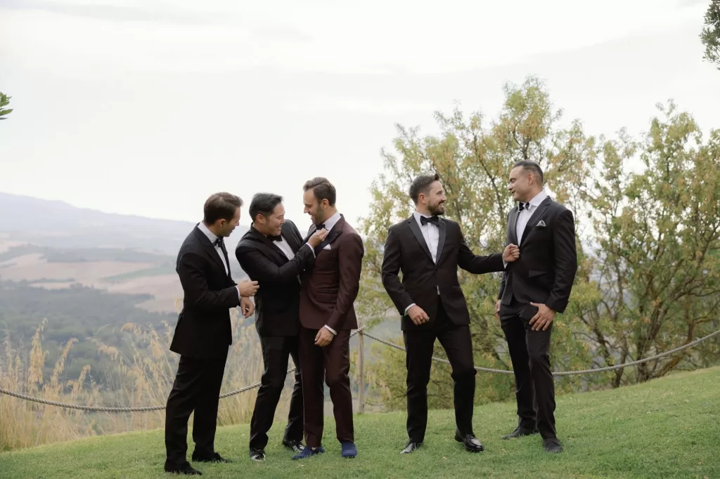 Groom sharing a relaxed moment with groomsmen against countryside views at Castello di Velona.