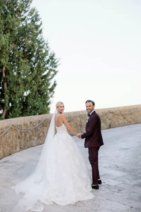 Bride and groom walking hand in hand through stone courtyard at Castello di Velona.