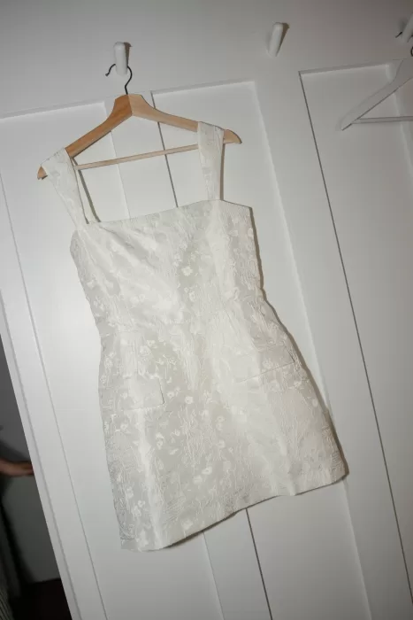 Modern bridal mini dress hanging on a wooden hanger inside Château Canet, showcasing intricate floral fabric and contemporary wedding styling.