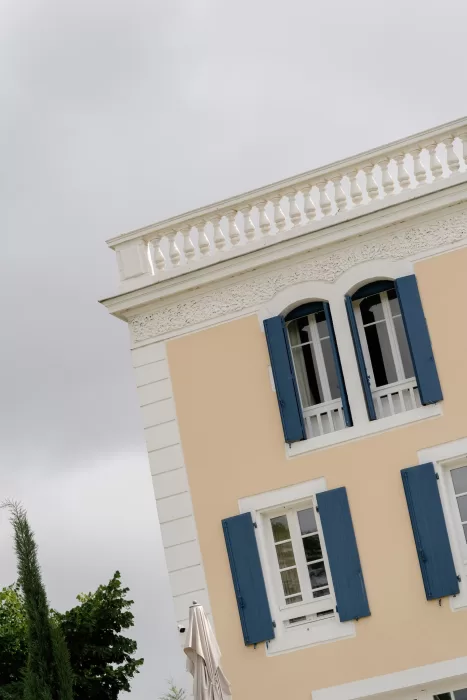 Architectural detail of Château Canet featuring cream stone walls, ornate balcony balustrades and signature blue shutters under a soft sky.