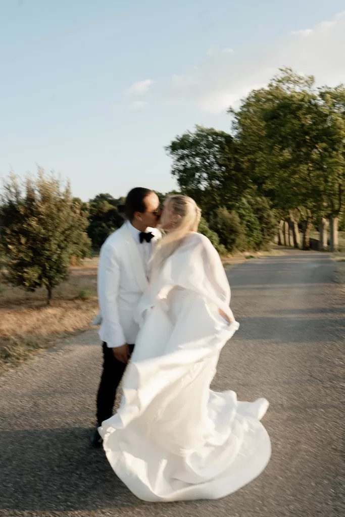 Bride and groom kissing on a quiet country road at Château Canet as the bride’s flowing cape catches the warm evening light.