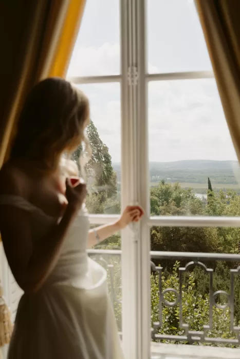 Bride looking out over the landscape from a window at Château du Prieuré d’Evecquemont, bathed in natural light.