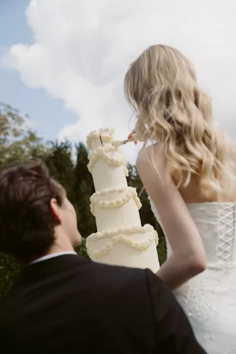 Close-up of the bride cutting the wedding cake outdoors at Château du Prieuré d’Evecquemont, captured from behind.