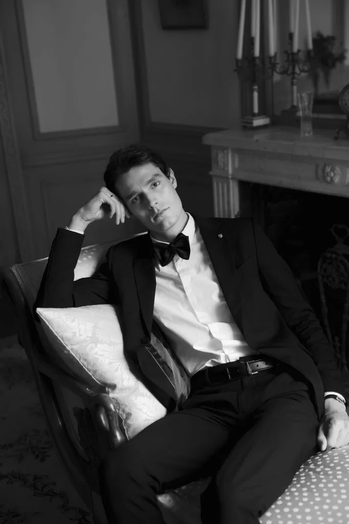 Black and white groom portrait reclining indoors at Château du Prieuré d’Evecquemont, calm and contemplative.