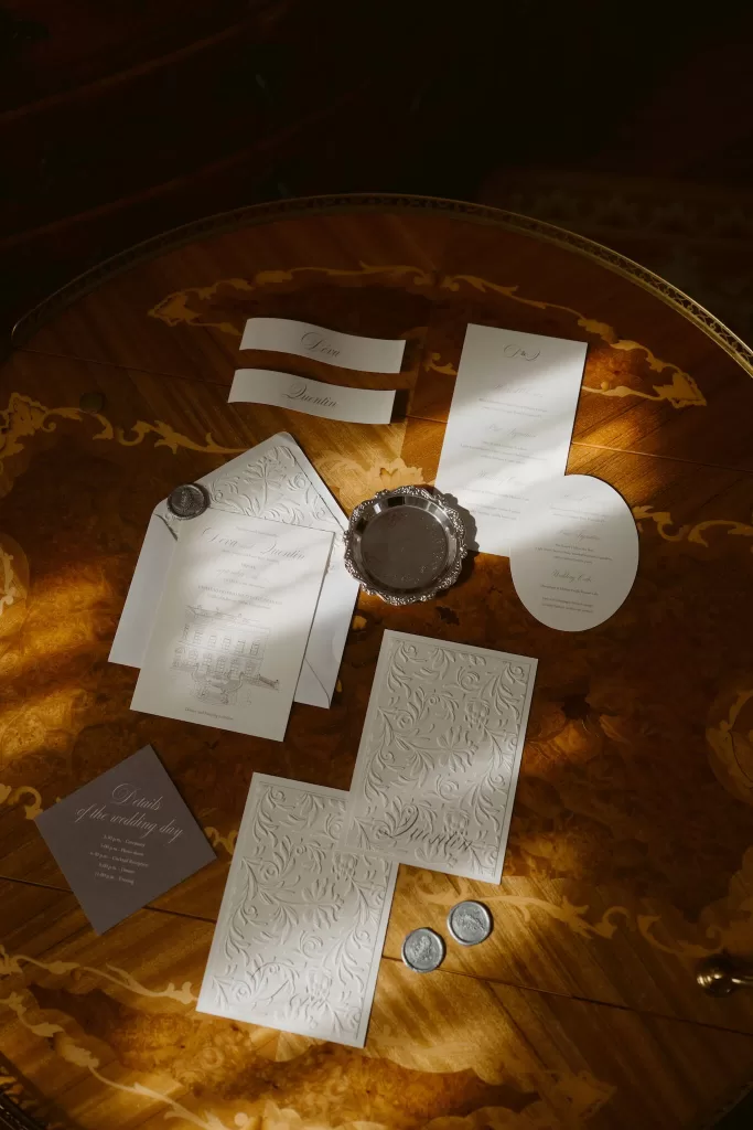 Wedding stationery suite styled on an antique wooden table at Château du Prieuré d’Evecquemont with warm, directional light.
