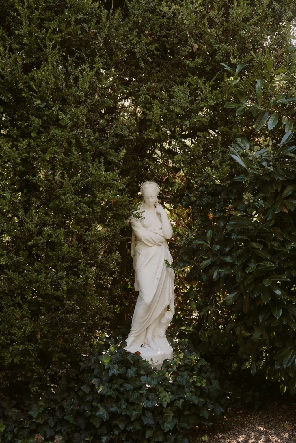 Classical garden statue framed by dense greenery at Château du Prieuré d’Evecquemont, creating a quiet, romantic atmosphere.