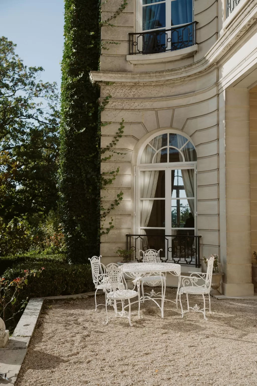 Outdoor terrace with wrought iron furniture at Château du Prieuré d’Evecquemont on a bright, calm day.