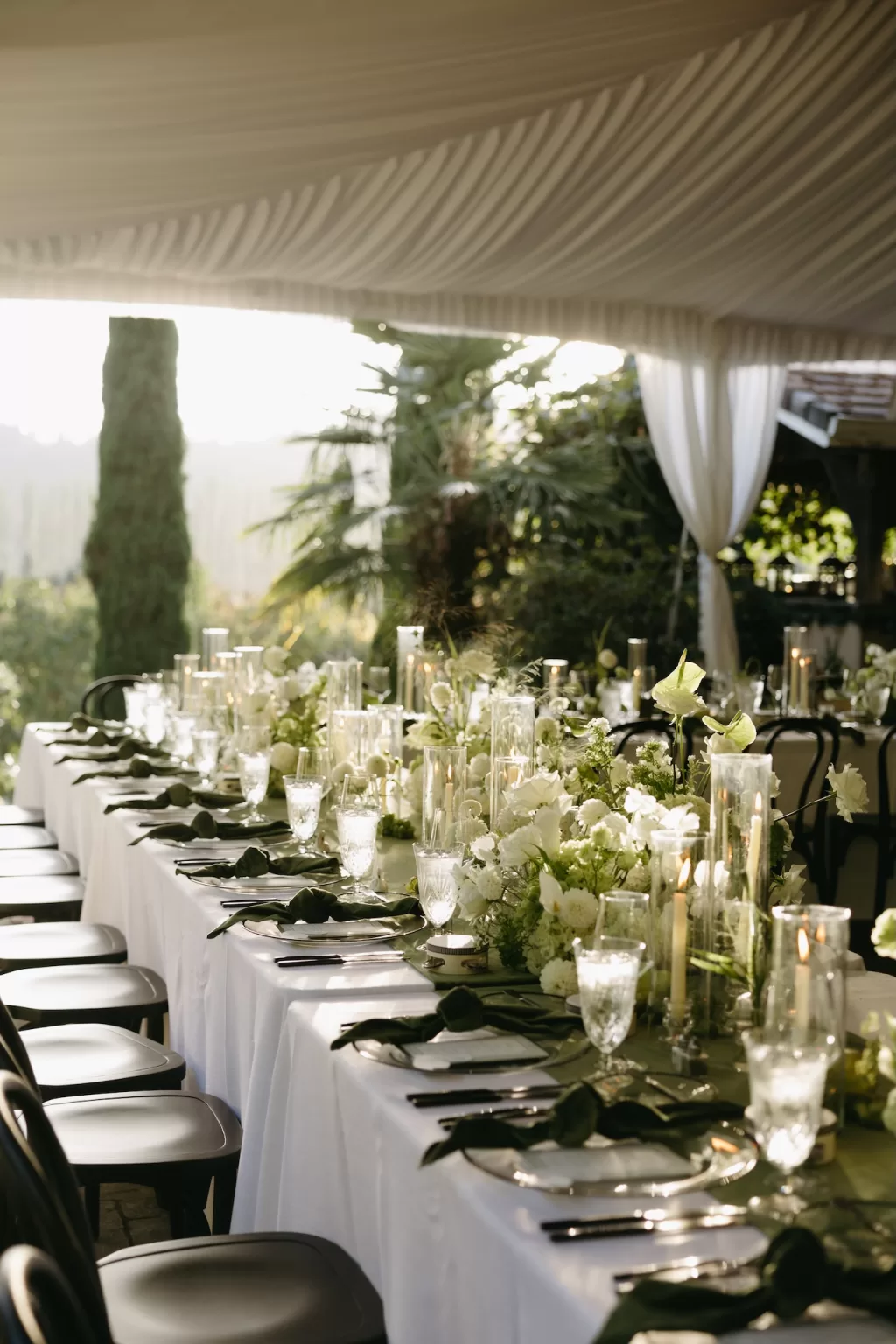 Refined wedding table details with green linens, white florals and glass candle holders under a marquee at Chateau Lill.