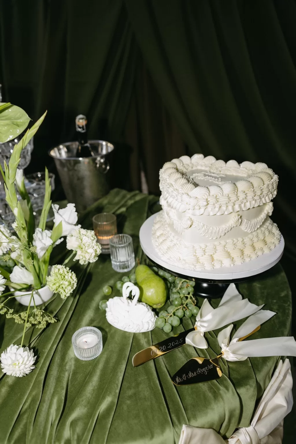 Wedding cake styled with green velvet linens, grapes and white florals during the reception at Chateau Lill.