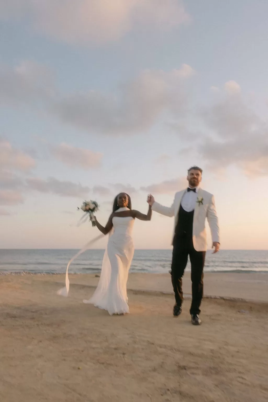 Bride and groom holding hands and walking joyfully along the sandy beach at Coral Residences.