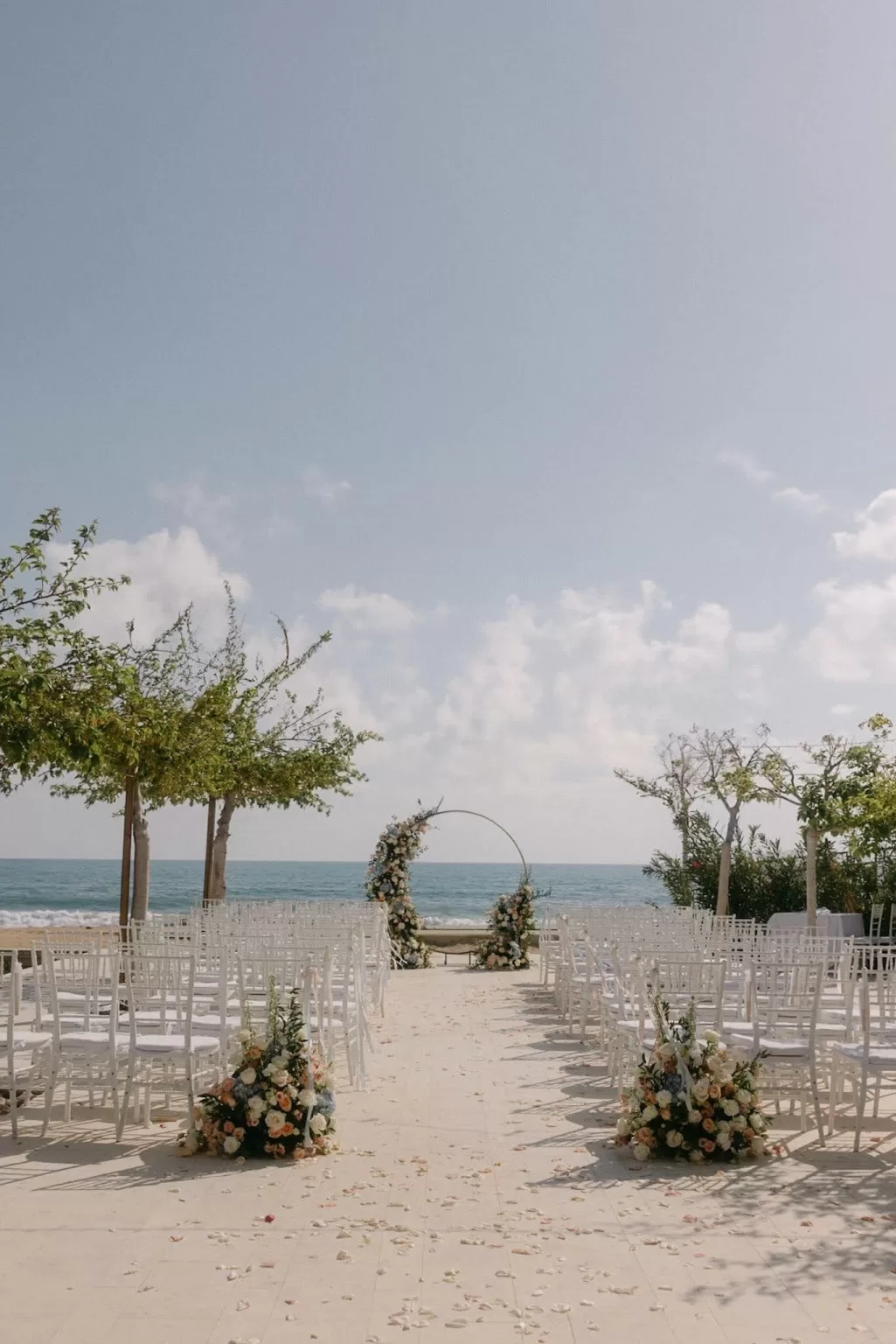 Elegant seaside ceremony setup with floral arch and white chairs at Coral Residences.