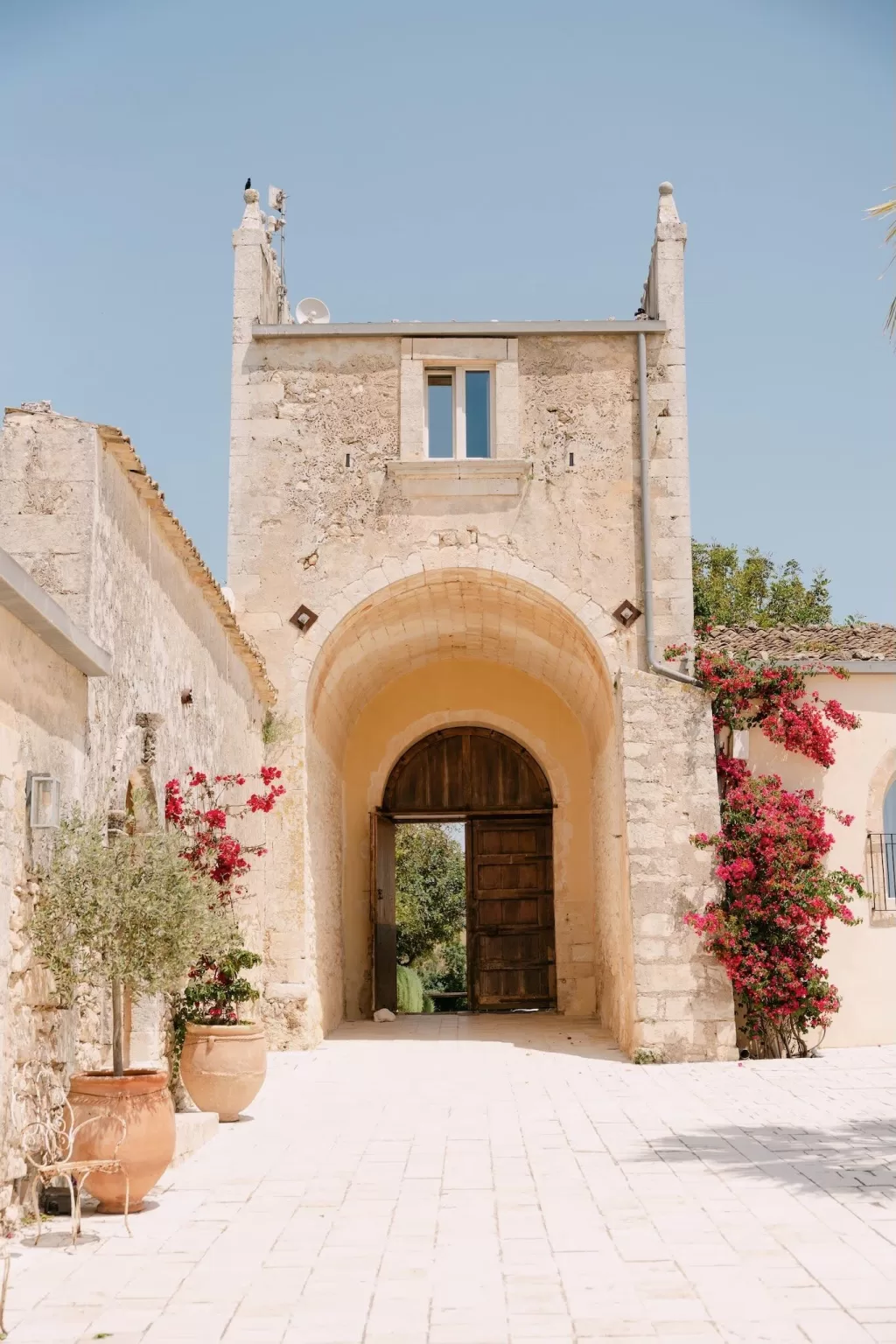 Historic stone archway entrance at Dimora Delle Balze framed by terracotta pots and blooming bougainvillea.