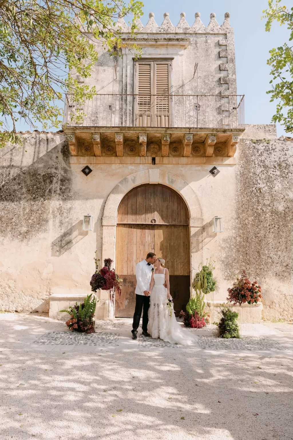 Bride and groom sharing a kiss beneath the grand entrance of Dimora Delle Balze surrounded by florals.