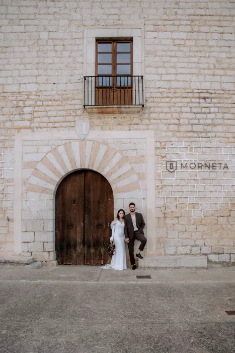 Bride and groom standing beneath the arched wooden doorway at Finca Morneta, framed by the historic stone architecture.
