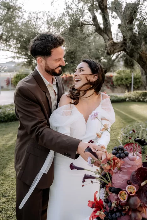 The couple cutting their wedding cake in the gardens of Finca Morneta, laughing together beneath olive trees.