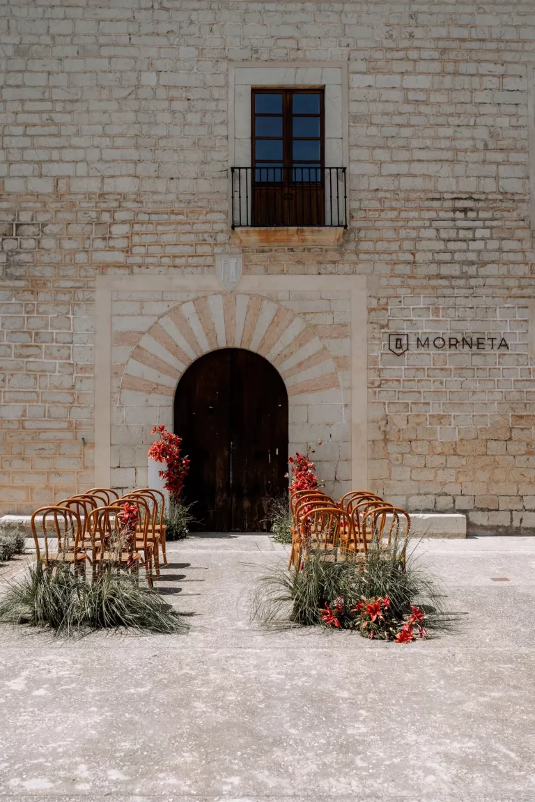 Outdoor wedding ceremony layout in the courtyard of Finca Morneta, rows of wooden chairs and red florals against the stone façade.