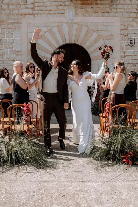 Bride and groom celebrating their ceremony exit at Finca Morneta, guests applauding between floral-lined chairs.
