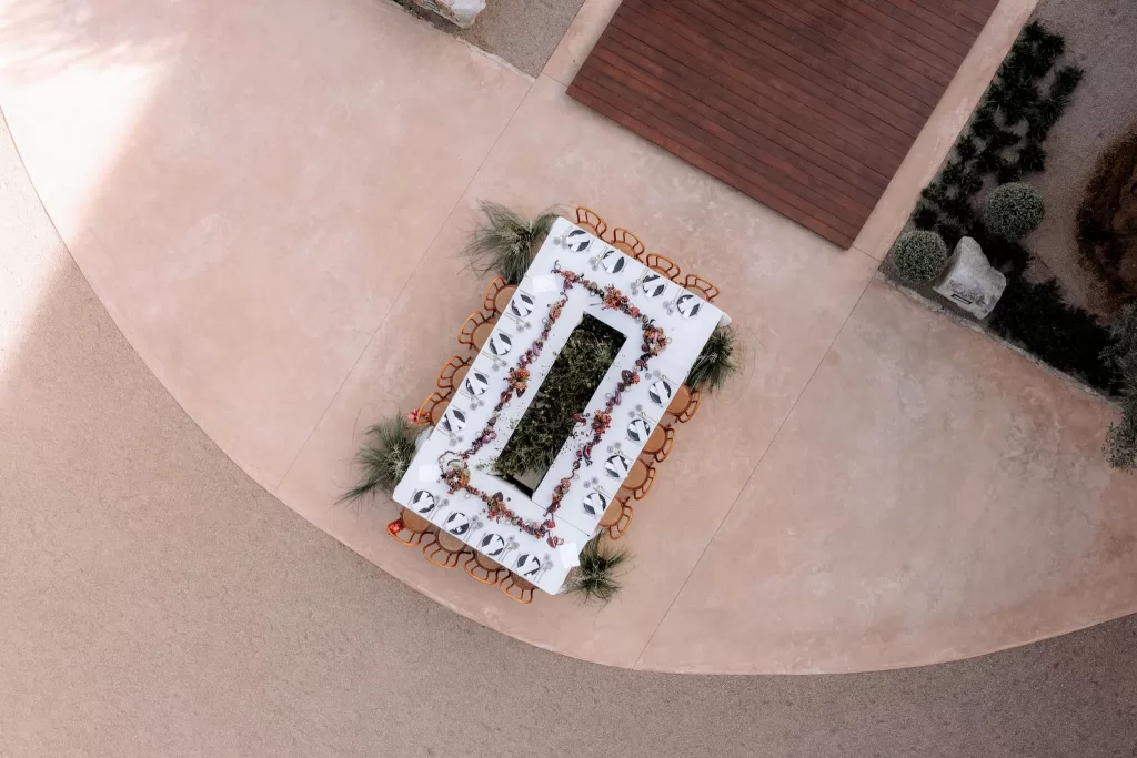 Overhead view of a long wedding reception table set in the courtyard of Finca Morneta with floral garlands and warm-toned chairs.