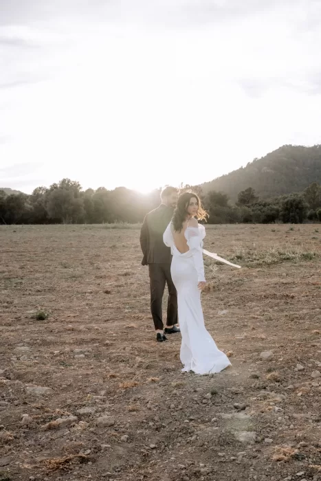 Bride and groom walking through open fields near Finca Morneta at sunset, backlit by warm Mallorcan light.