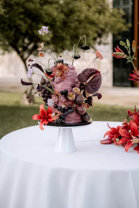 Artistic wedding cake at Finca Morneta decorated with fresh fruit, deep red blooms and sculptural florals.