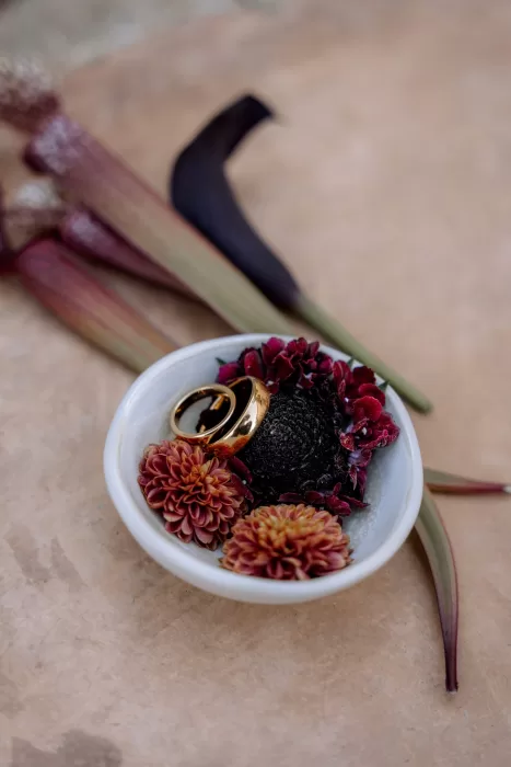 Gold wedding rings resting in a small ceramic bowl with rich red florals at Finca Morneta, styled in warm earthy tones.