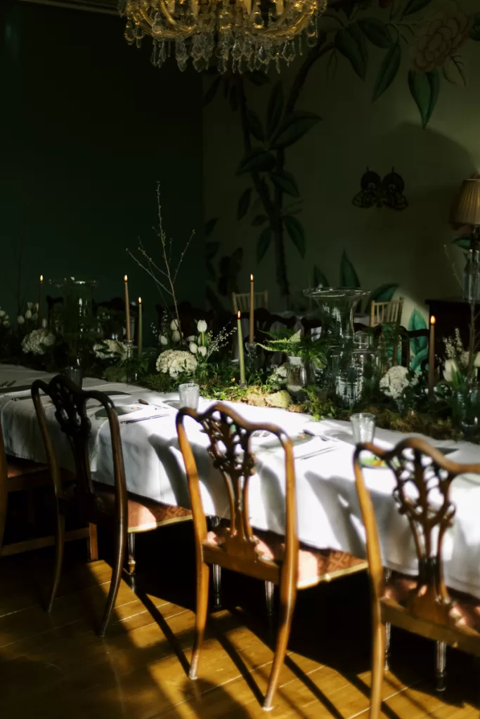 Intimate candlelit dining setup inside Garthmyl Hall, with greenery-lined tables and soft evening light creating a moody atmosphere.